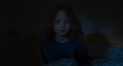 a young girl sitting on a bed in a dark room
