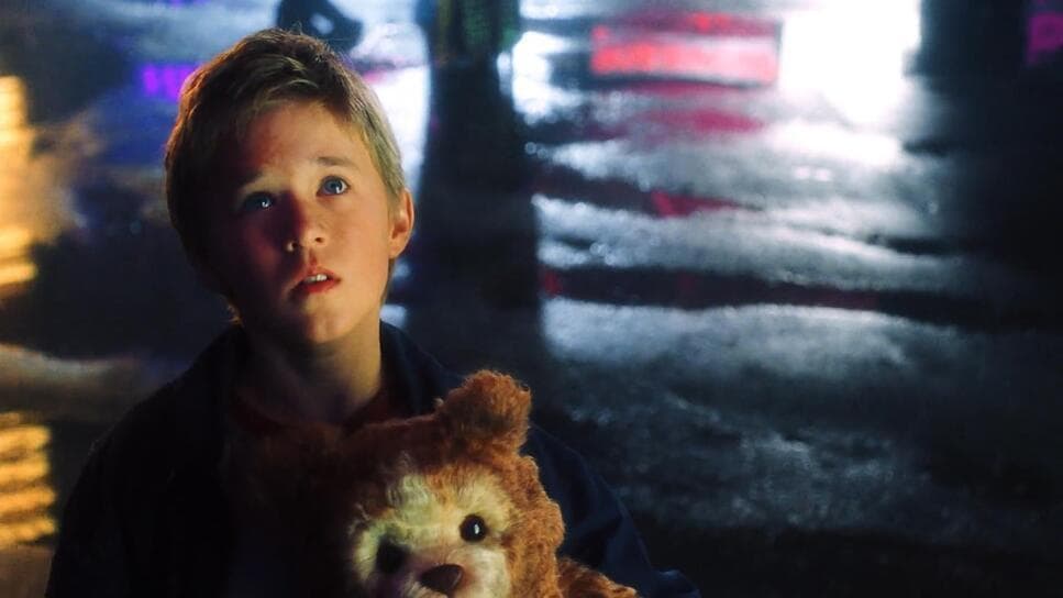 a young boy holding a teddy bear in the rain