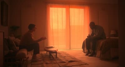a couple of men sitting in a living room next to a window