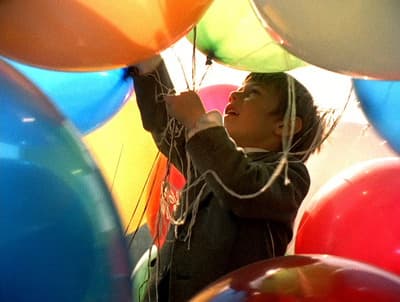 a young boy holding onto a bunch of balloons