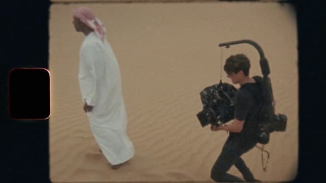 a man walking across a desert holding a camera
