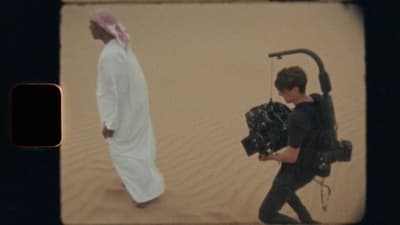 a man walking across a desert holding a camera