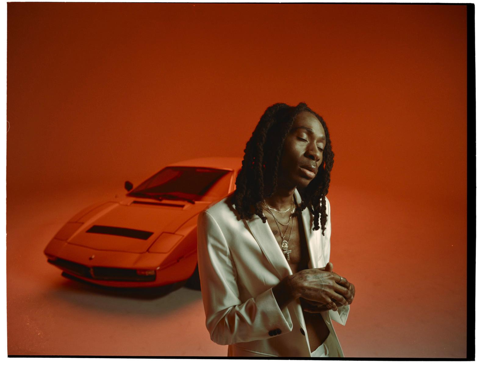 a man with dreadlocks standing next to a car
