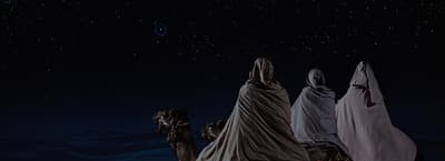 a group of people standing on top of a hill under a sky filled with stars