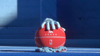a hand holding a red ball on top of a tennis court