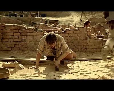 a man kneeling down on the ground next to a brick wall