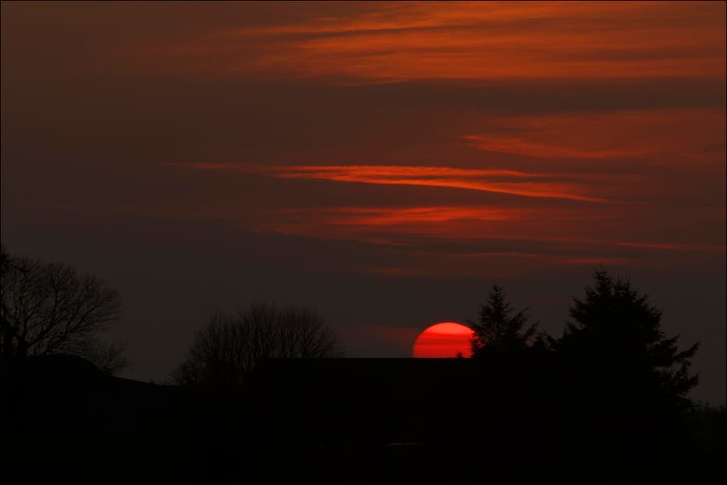 the sun is setting in the sky behind some trees