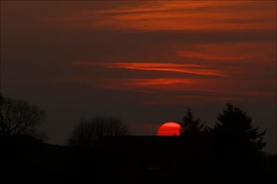 the sun is setting in the sky behind some trees