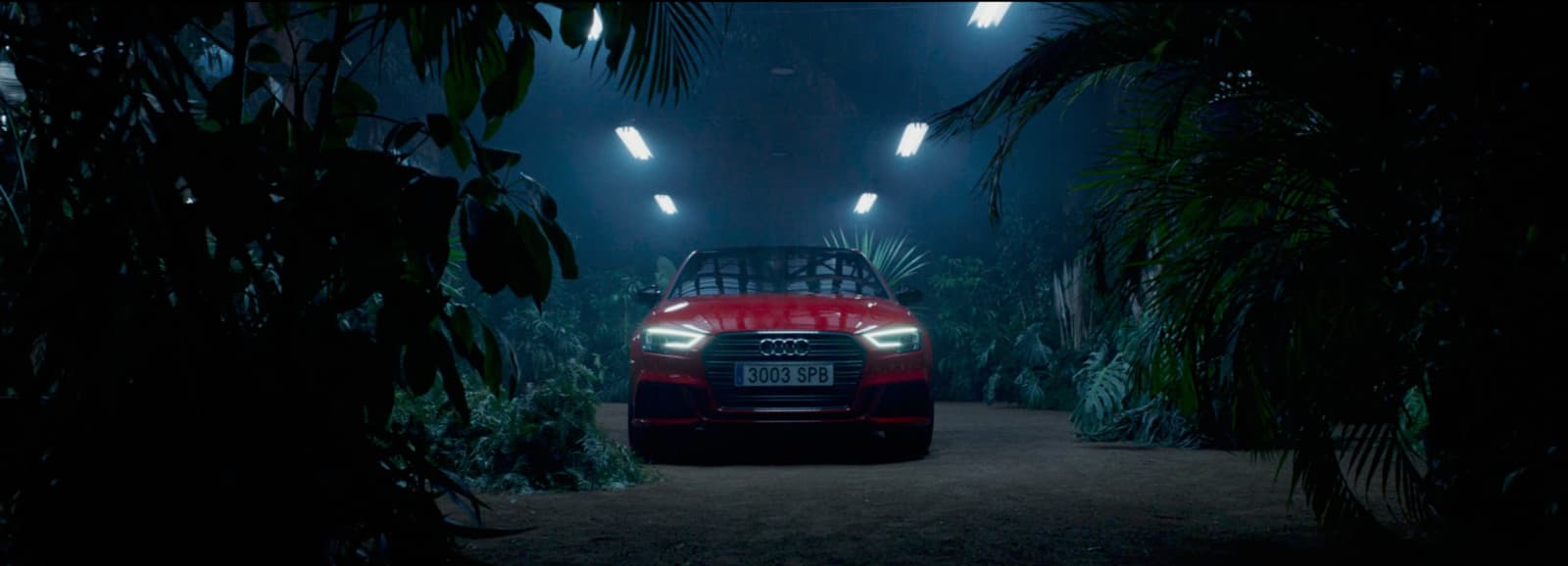 a red car driving through a forest at night