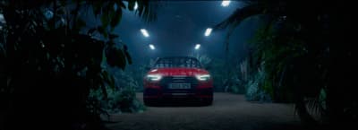a red car driving through a forest at night
