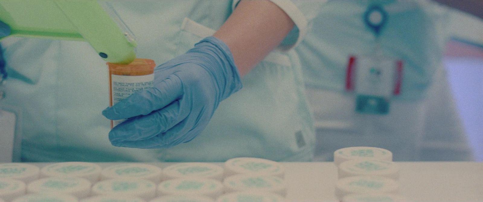 a person in blue gloves holding a bottle of medicine