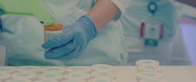 a person in blue gloves holding a bottle of medicine