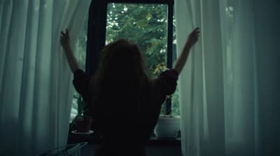 a woman standing in front of a window with her arms up
