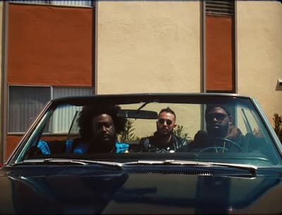 three men sitting in a car in front of a building