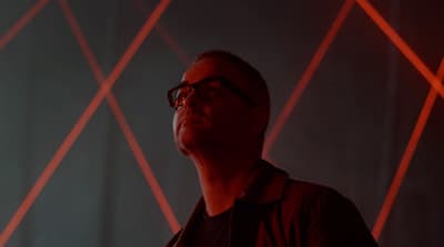a man with glasses standing in front of a red light