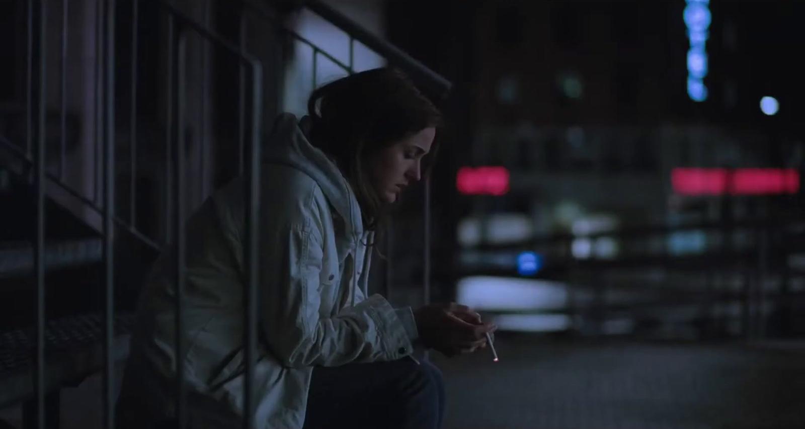 a woman sitting on a ledge with a cigarette in her hand
