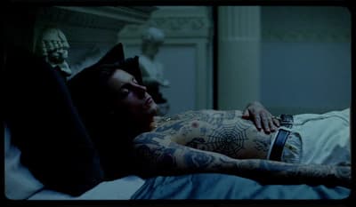 a man laying in bed with tattoos on his arms
