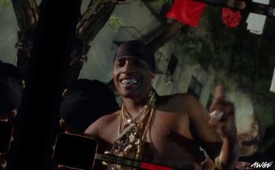 a man wearing a necklace and a hat standing in front of a group of people