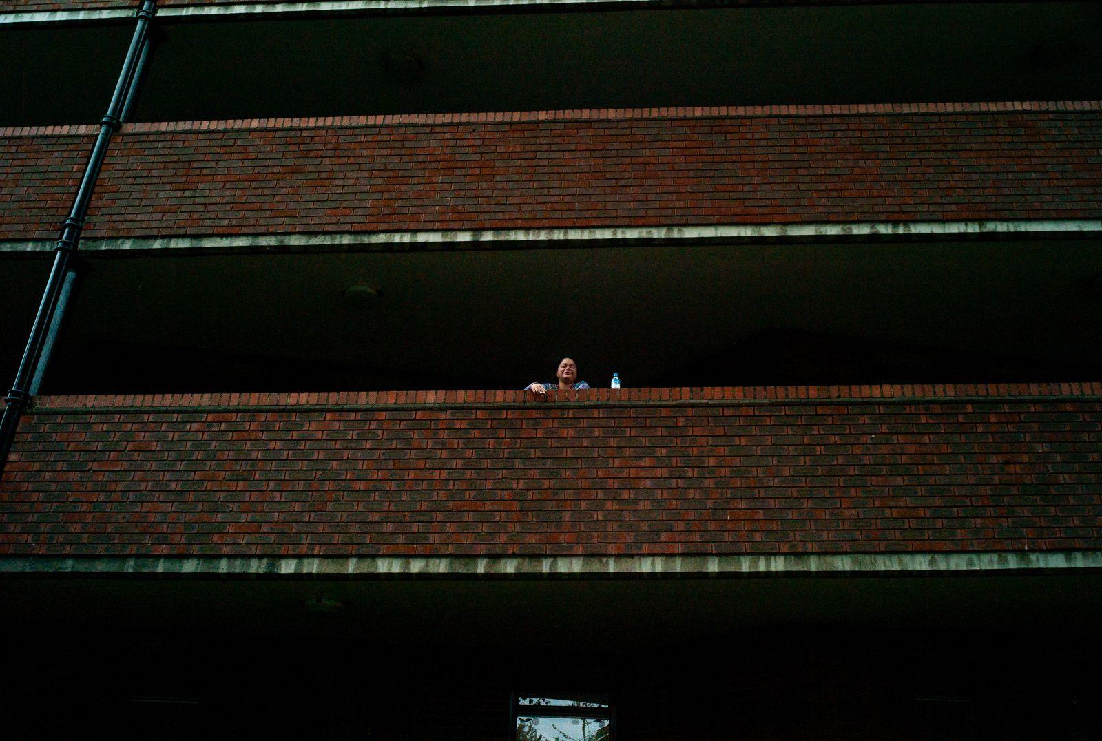 a woman standing on a balcony next to a brick building