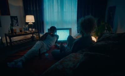 two people sitting on a bed in a dark room