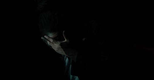 a man in the dark covering his face with his hands