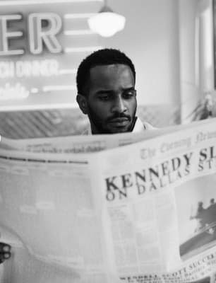 a man reading a newspaper while sitting at a table