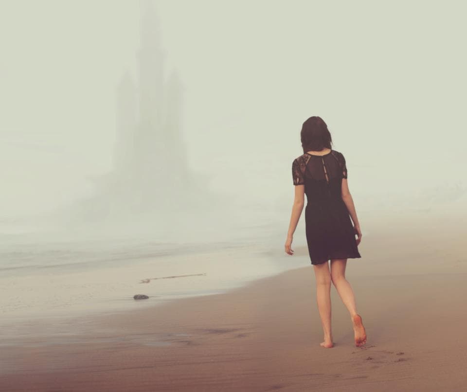 a woman in a black dress walking on a beach