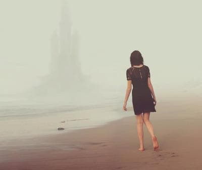 a woman in a black dress walking on a beach