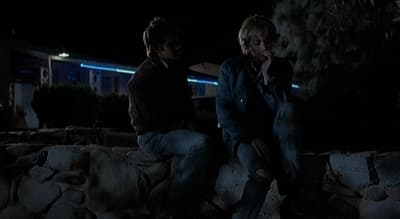 two people sitting on a rock wall at night