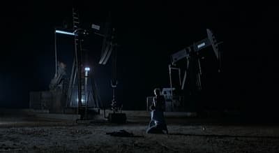 a person walking in the dark near some oil pumps