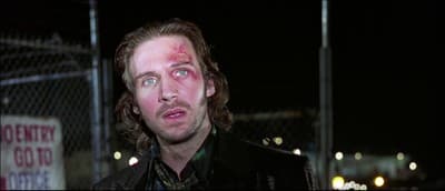 a man with a bloody face standing in front of a fence