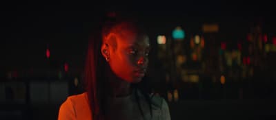 a woman standing in the dark with a city in the background