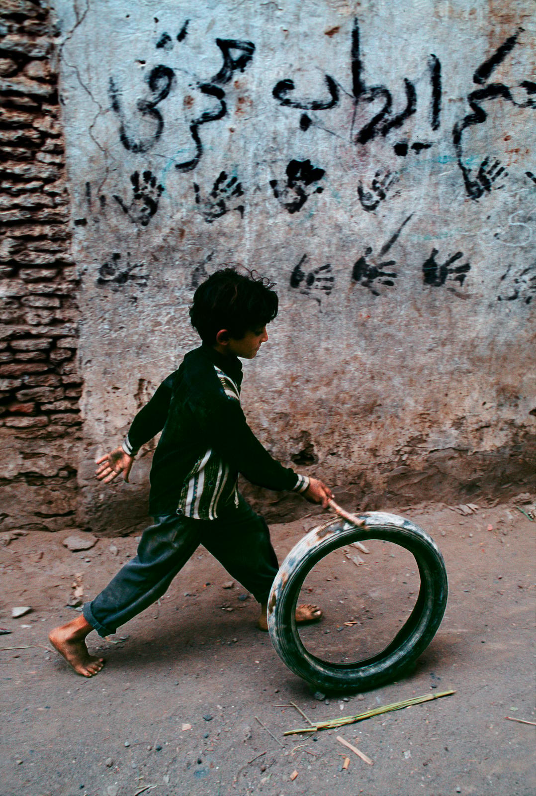 a young boy pushing a tire down a street