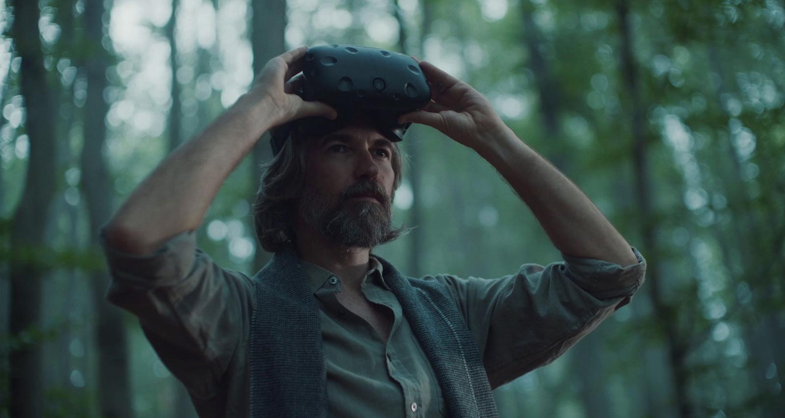 a man with a beard holding a camera in the woods