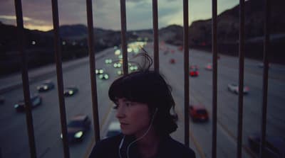 a woman listening to music while standing in front of a fence