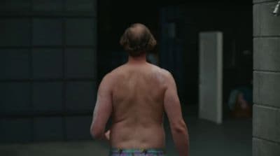 a man with no shirt walking down a hallway