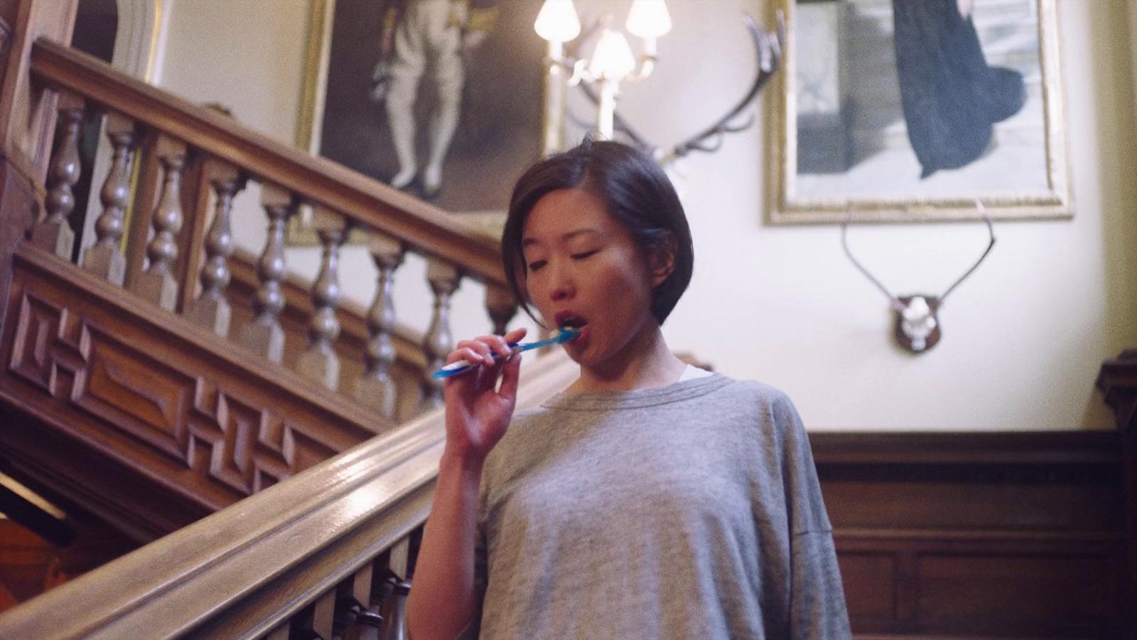 a woman brushing her teeth in front of a staircase