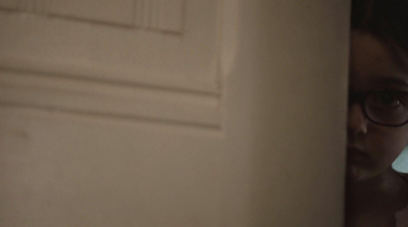 a young girl wearing glasses looking through a door