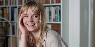 a woman sitting in front of a bookshelf smiling