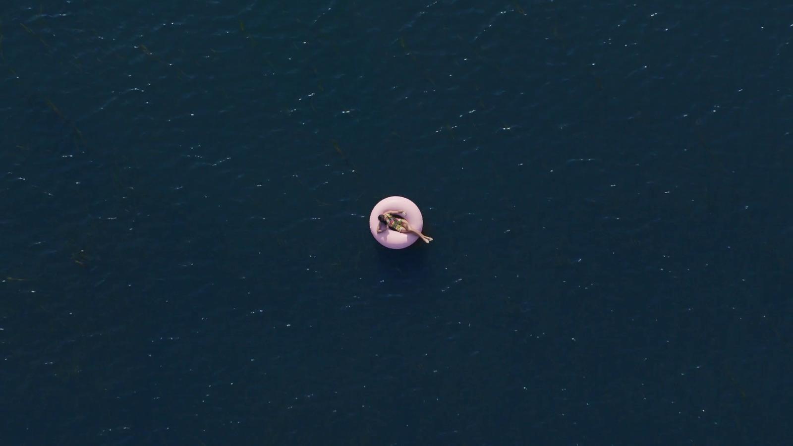 an aerial view of a person floating on a pink object in the water