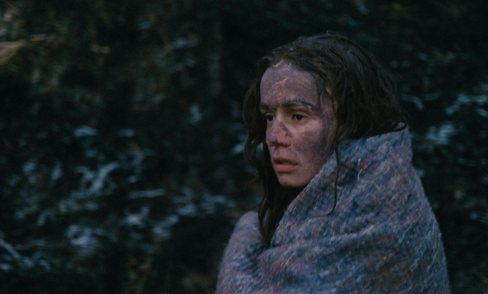 a woman wrapped in a blanket in front of trees