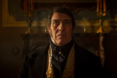 a man in a suit and tie standing in front of a fireplace