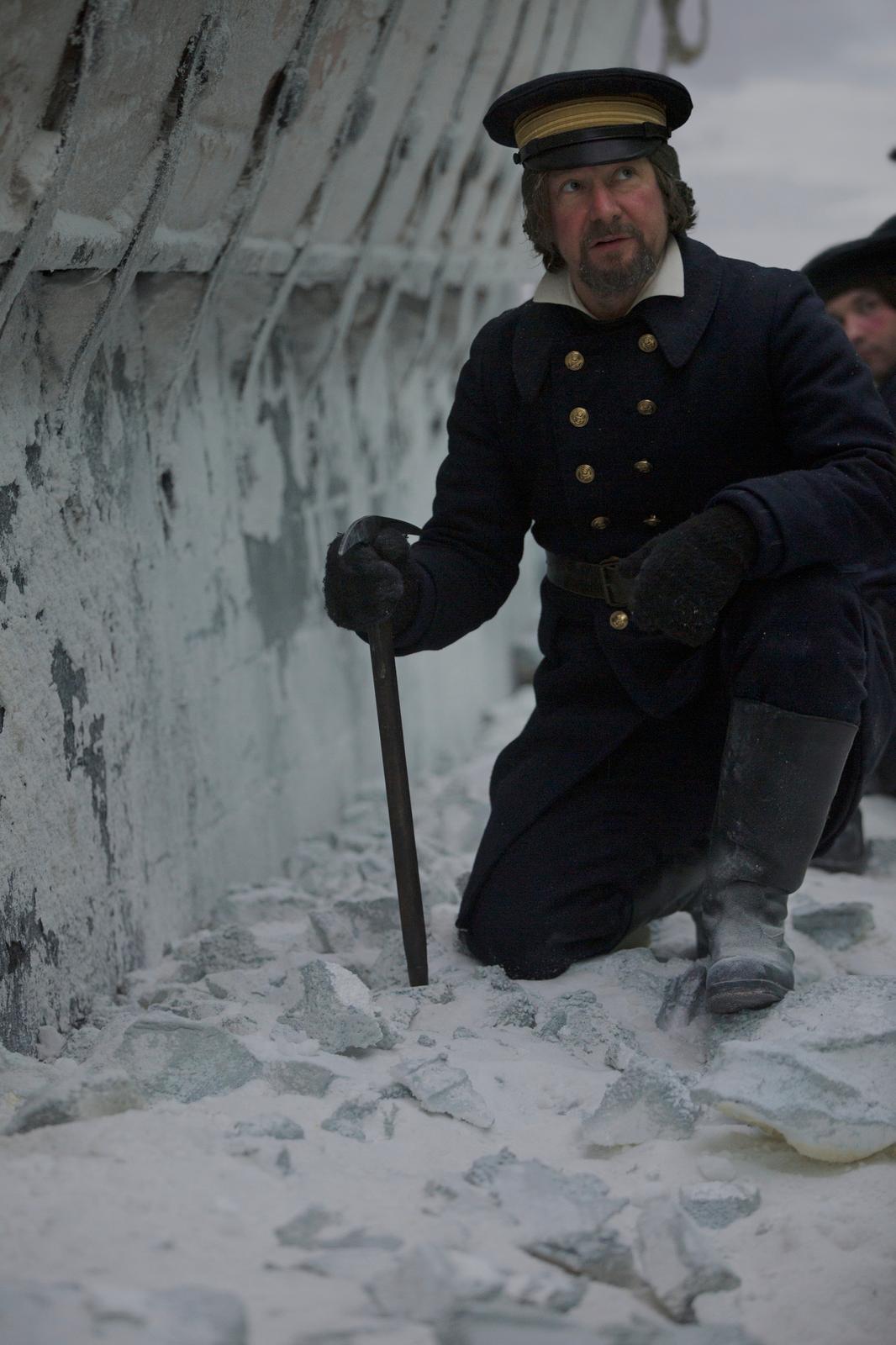 a man kneeling down in the snow with a cane