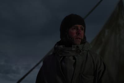 a man in a jacket and hat standing in front of a tent