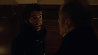 a man looking at another man in a dark room