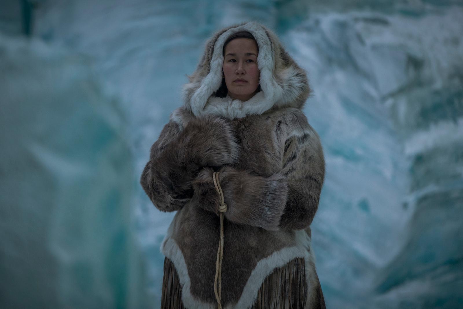 a woman in a fur coat standing in front of a glacier