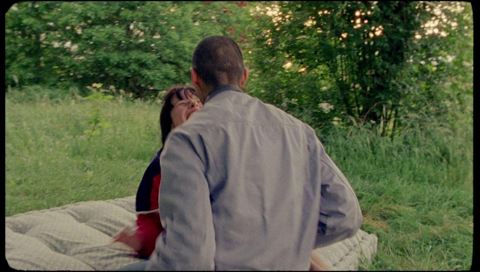 a man and woman sitting on a blanket in the grass