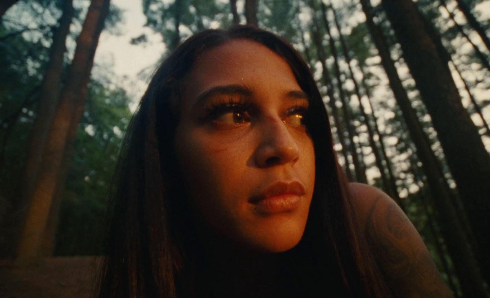 a woman standing in a forest with trees in the background