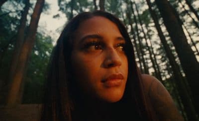 a woman standing in a forest with trees in the background