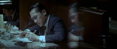 a man sitting at a table writing on a piece of paper
